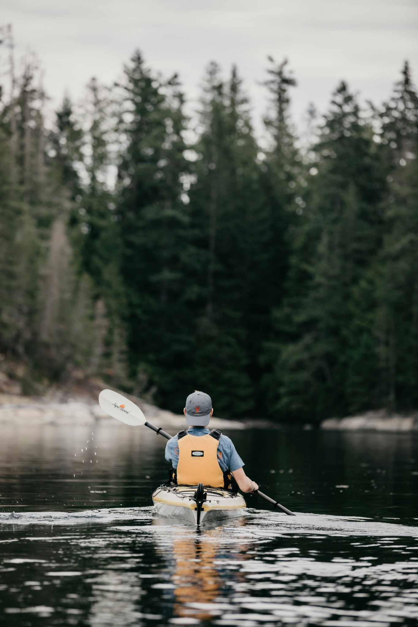 A paddler kayaking on calm water surrounded by forest